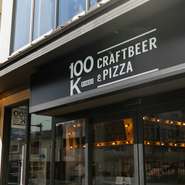 下京区真苧屋町に2023年9月にオープンした【CRAFTBEER&PIZZA 100K】は、クラフトビールとピザが自慢のイタリアン酒場。ハイスツールが並ぶ開放的な空間で、スタイリッシュな時間を堪能できるお店です。
