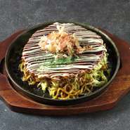 お好み焼きと焼きそばを合わせた関西のソウルフード！太麺の焼きそばとお好み焼きの生地を卵でつなぎ、ボリューム感あふれる見た目と、それに違わない食感が特徴の逸品となっています。　
