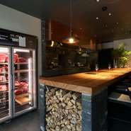 ライブ感溢れるオープンキッチンで炭＆薪の音やゲストが談笑する声、グラスの音が響きます。上質な空間の中にどこかホッとするような居心地の良さも魅力。焼き師がベストな焼き方で厳選牛を焼き上げます。
