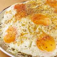 千切りキャベツの上に7個までのお好みの個数のおお目玉焼きをのせることができる豪快なおつまみ！カレー粉・魚粉・黒胡椒で味付けされたやみつきなる一品です！