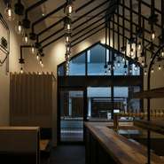 駅近の好立地ながら、大通りから一本入ったビル1階に佇み、隠れ家感が高い店。ロッジ風の空間に配した登り梁状の照明、左官仕上げの美しい塗り壁、丸太のオブジェなど、都心にいながら自然の温もりを感じられます。