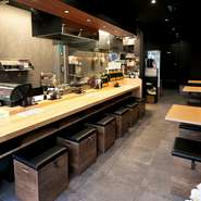 入り口側の壁面は全面ガラス張りで入りやすく明るい雰囲気。店内はカウンター席をメインにテーブル席も備えています。内装は黒を基調としたモダンなイメージ。オープンキッチンのため調理のライブ感も楽しめます。