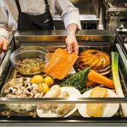 食材を前に、安達シェフの説明を聴きながらその日のメニューを決めていくのが、この店のスタイル。スモークサーモンはサラダ仕立てで、手前の豚足はパン粉焼きにと、できる限り好みの調理法で仕上げてくれる。