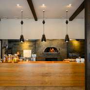 重厚感のある石造りの玄関を抜けると、石窯の炎と香りが出迎えてくれます。オープンキッチンに立つ2人のシェフの掛け合いを見ながら楽しむ、贅沢な食事時間。福井の風景や文化を感じる、特別な空間です。