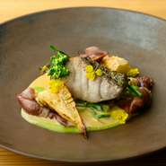 コースの魚料理には、旬の魚を使用しています。春はスズキ。薪火を使い短時間で焼き上げ、魚の旨みを閉じ込めているのが特長です。春野菜とホタルイカを添え、豆のソースで水分を逃がさずに仕上げました。