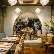 コンクリートの壁に温かみを添える植物や、籐家具などオリエンタルなインテリアが配され、リラックスムードが漂う店内。アーチ状の壁から見えるオープンキッチンは一枚の絵画のようにフォトジェニック。