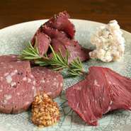 北海道や岐阜県で獲れた野生肉を丁寧迅速に解体、下処理を行い提供されるジビエメニュー。燻製ハム・パストラミ・ボロニアソーセージの3種を盛り合わせにした一皿です。大自然が育む凝縮された旨みに舌鼓。
