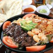 オリジナルソースでマリネした牛・豚・鶏肉を鉄板焼いた『ファヒータ』。サワークリームやアボカドをたっぷり乗せてトルティーヤで巻く人気メニュー。オーダーが入ってから1枚ずつやくトルティーヤも絶品。