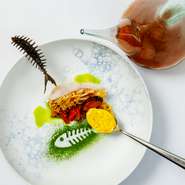 海をイメージしたお皿に描かれたアオサノリの緑の魚、じゃが芋とイカ墨を合わせた魚型の黒いチップス、鮮やかな黄色のサフランムース。まるでアートのような一皿は、味わい深い魚介スープを注いで完成します。